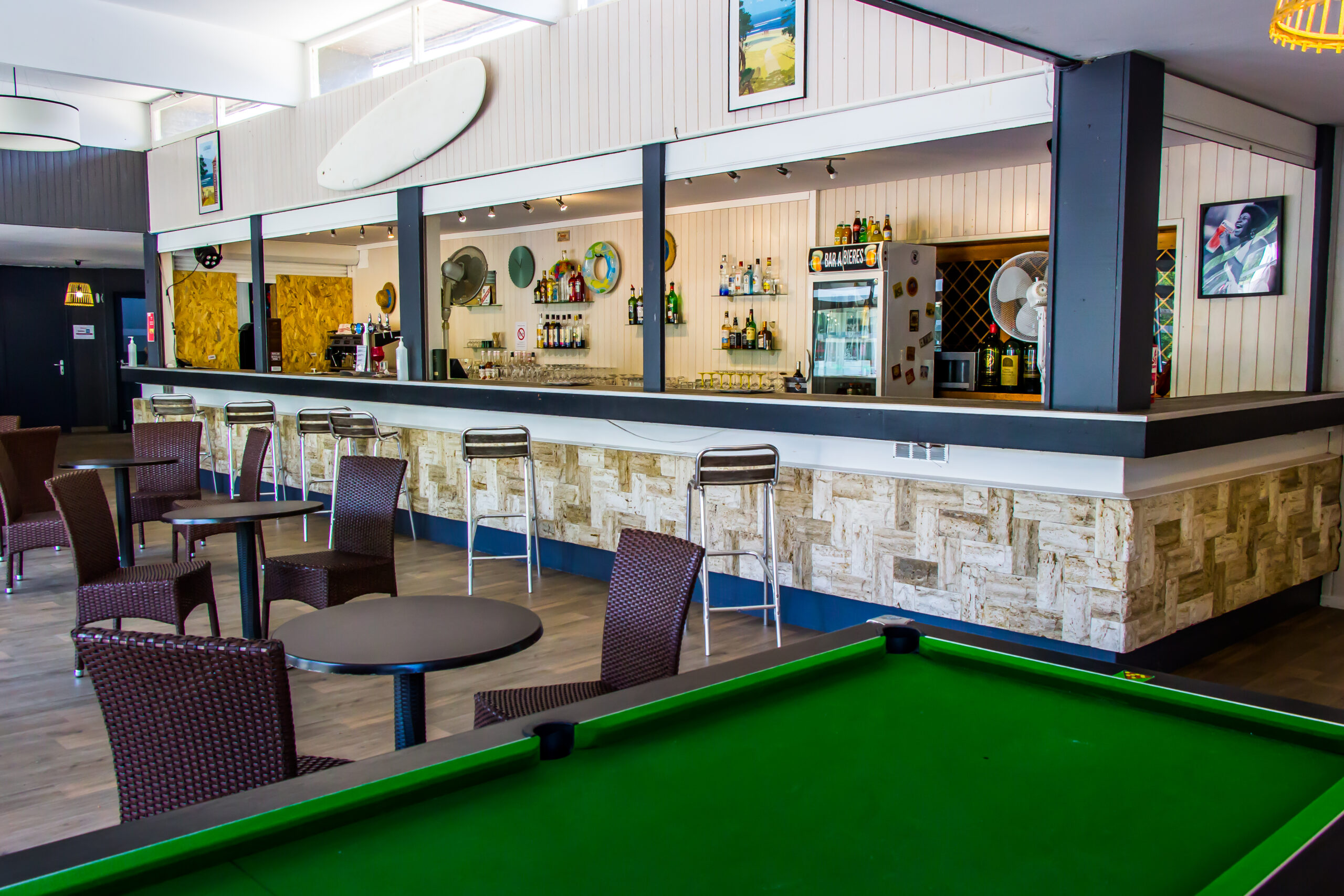 Intérieur d'un bar avec tables, chaises, tabourets hauts et un billard vert au premier plan