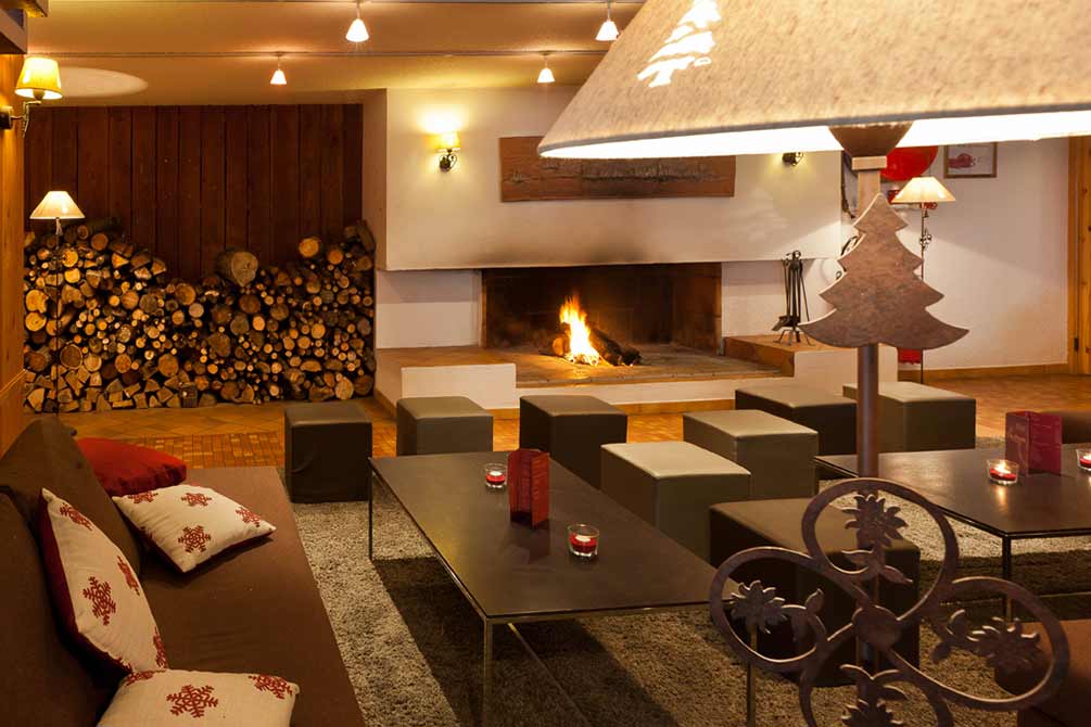 Salon cosy avec grande cheminée allumée, décoration montagnarde et atmosphère chaleureuse pour l'après-ski
