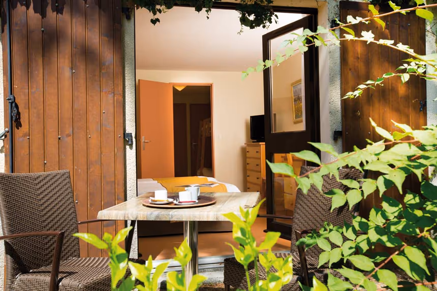Chambre avec terrasse privée aménagée, table de petit-déjeuner et fauteuils en rotin entourés de verdure