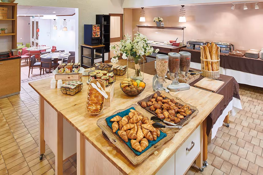 Buffet de petit-déjeuner généreux avec viennoiseries fraîches, céréales, fruits et produits variés dans une salle lumineuse
