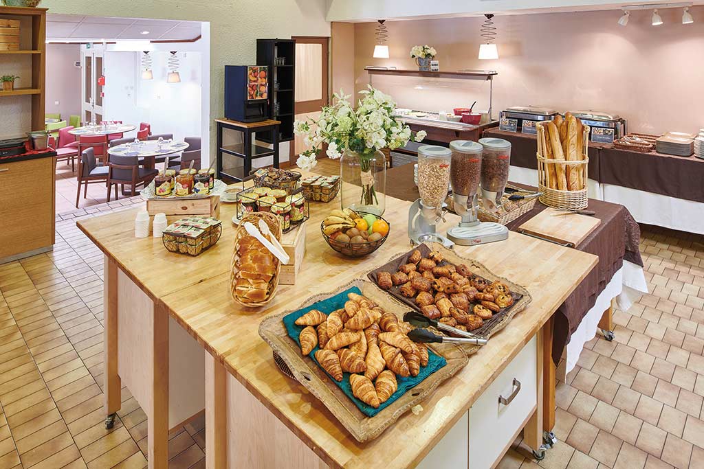 Buffet de petit-déjeuner généreux avec viennoiseries fraîches, céréales, fruits et produits variés dans une salle lumineuse