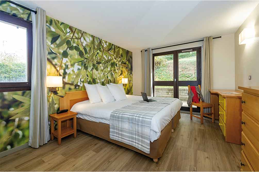 Chambre Azureva spacieuse avec papier peint immersif représentant un olivier, lit double confortable et accès terrasse