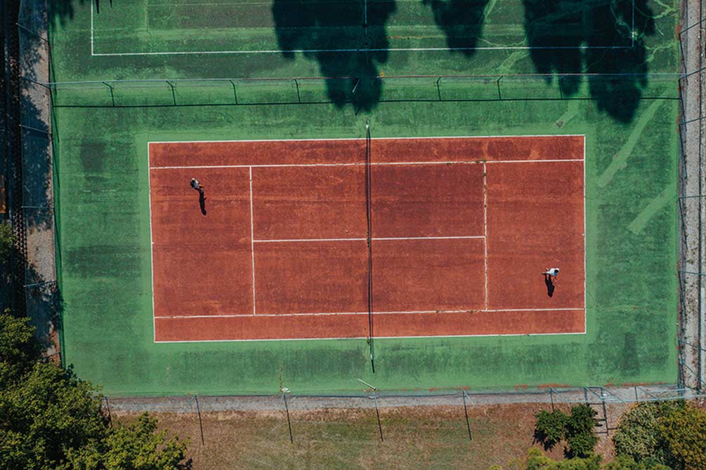 Vue aérienne d'un court de tennis en terre battue d'un Village Vacances Azureva avec deux joueurs en pleine partie