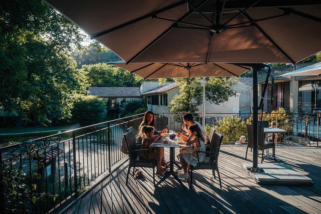 Famille partageant un repas sur une terrasse en bois au coucher du soleil, ambiance chaleureuse et conviviale