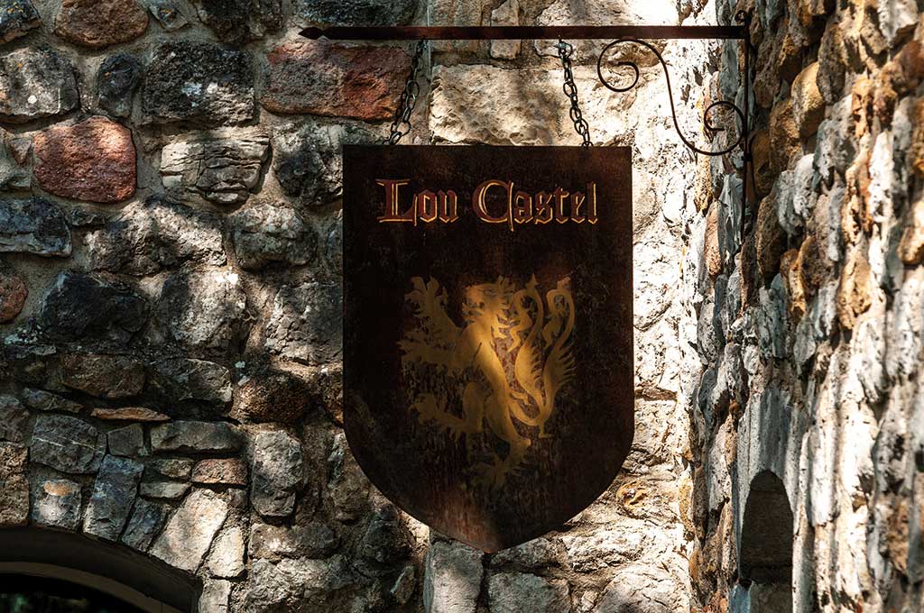 Enseigne historique en métal "Lou Castel" accrochée sur un mur en pierres anciennes