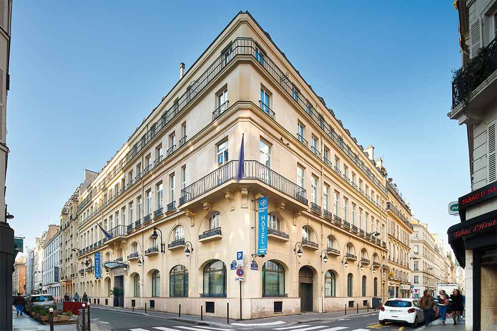 Façade élégante de l'hôtel Azureva à Paris avec architecture haussmannienne, arches en pierre et balcons typiques parisiens