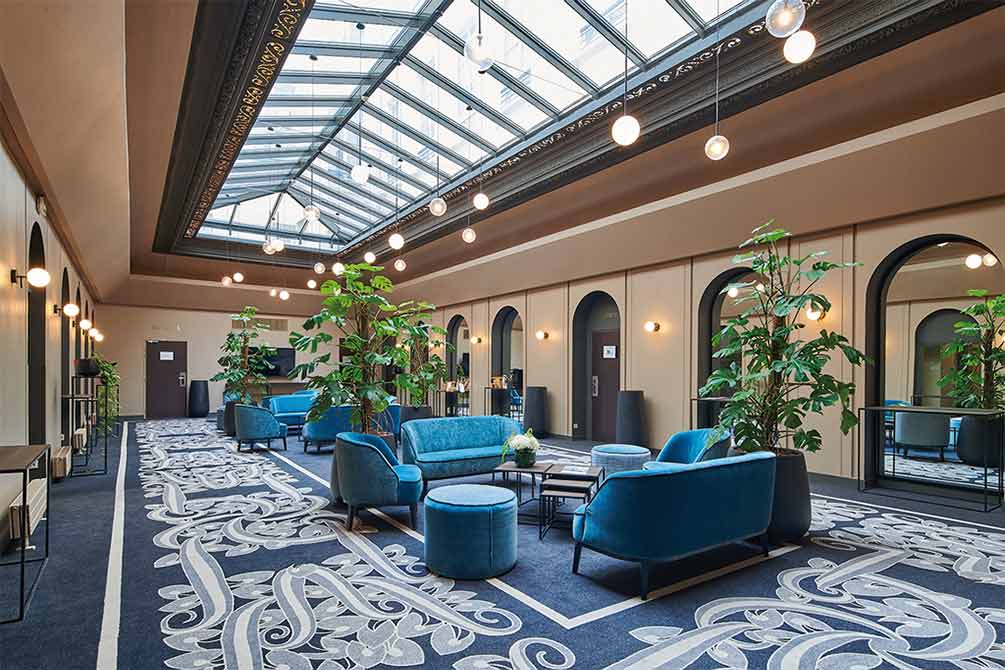 Hall d'hôtel Azureva à Paris avec grande verrière, mobilier velours bleu élégant, plantes vertes et décoration raffinée