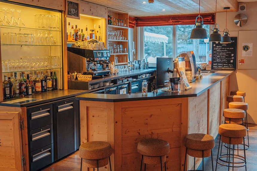 Bar convivial d'un établissement Azureva en montagne avec comptoir en bois, tabourets chaleureux et décoration d'inspiration montagnarde
