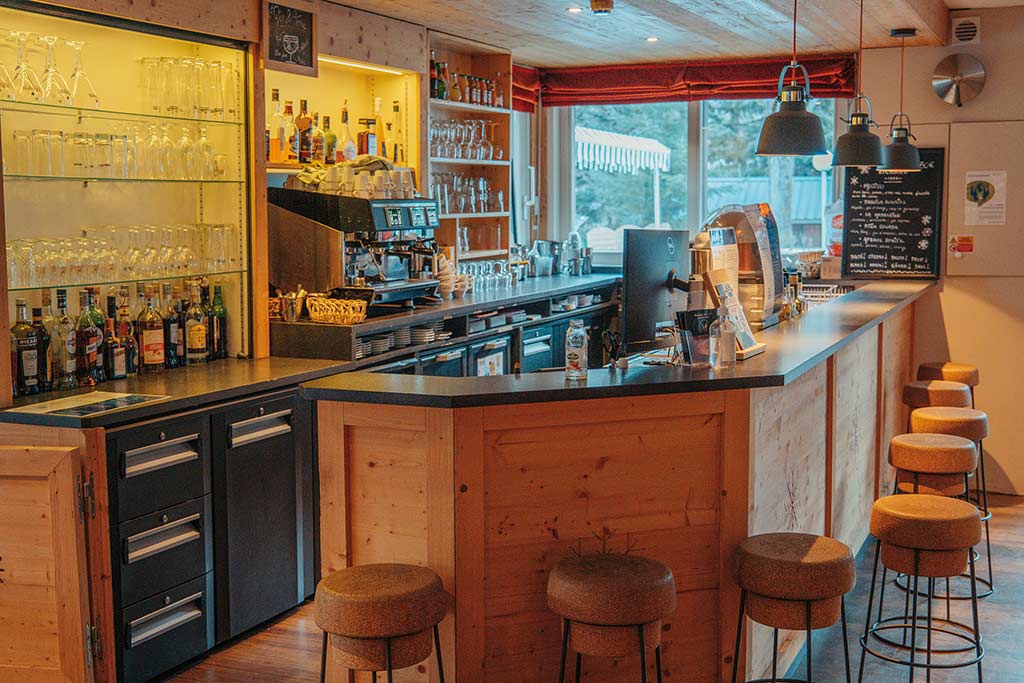 Bar convivial d'un établissement Azureva en montagne avec comptoir en bois, tabourets chaleureux et décoration d'inspiration montagnarde