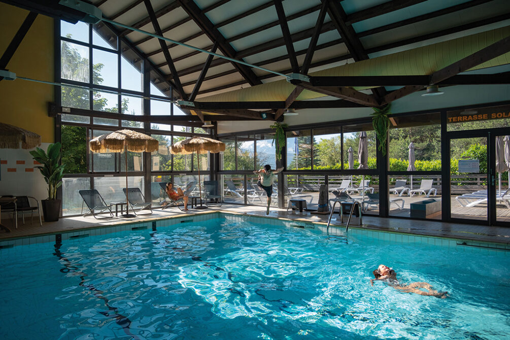 Piscine intérieure couverte avec baies vitrées et espace détente au village vacances