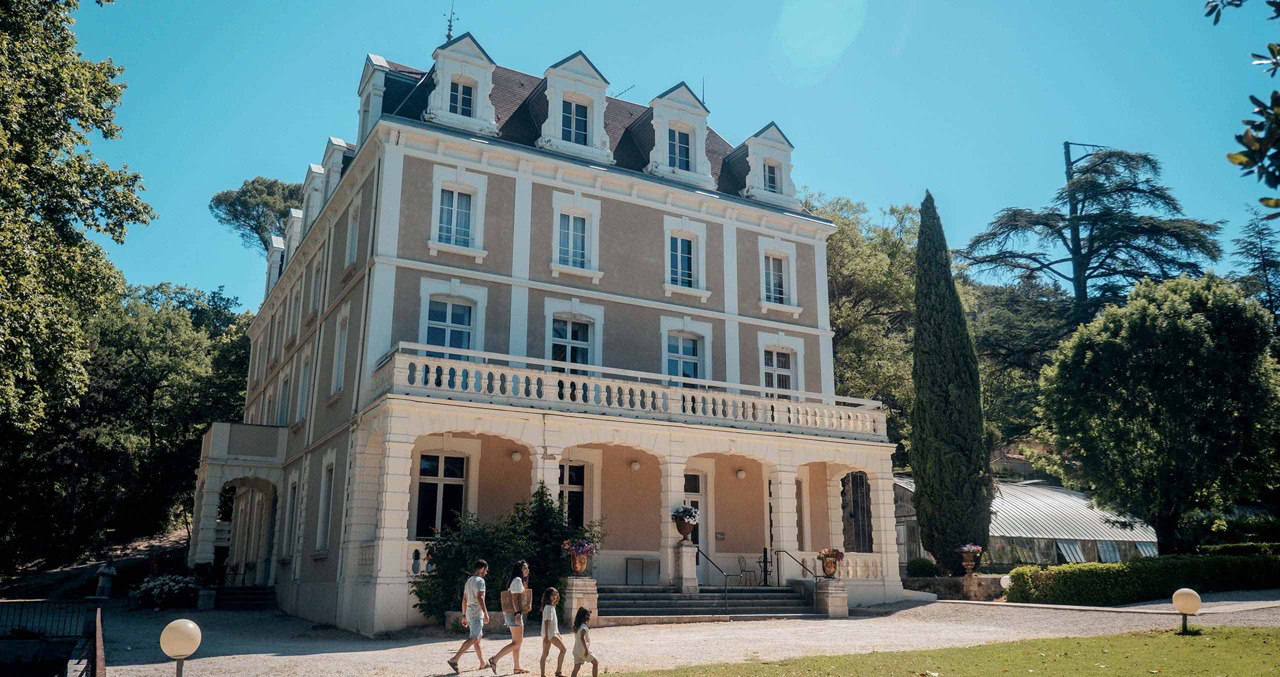 Famille se promenant devant un hôtel Azureva installé dans une demeure de caractère avec architecture classique, entourée d'un parc arboré