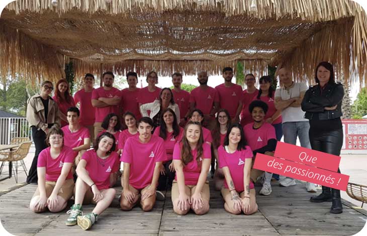 Équipe d’animation Azureva souriante en t-shirts roses, réunie sur un village vacances sous un auvent en bois