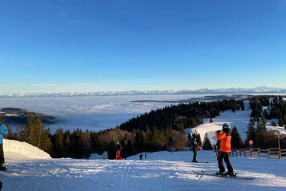Skieurs sur les pistes enneigées avec vue Métabief et une mer de nuages en hiver