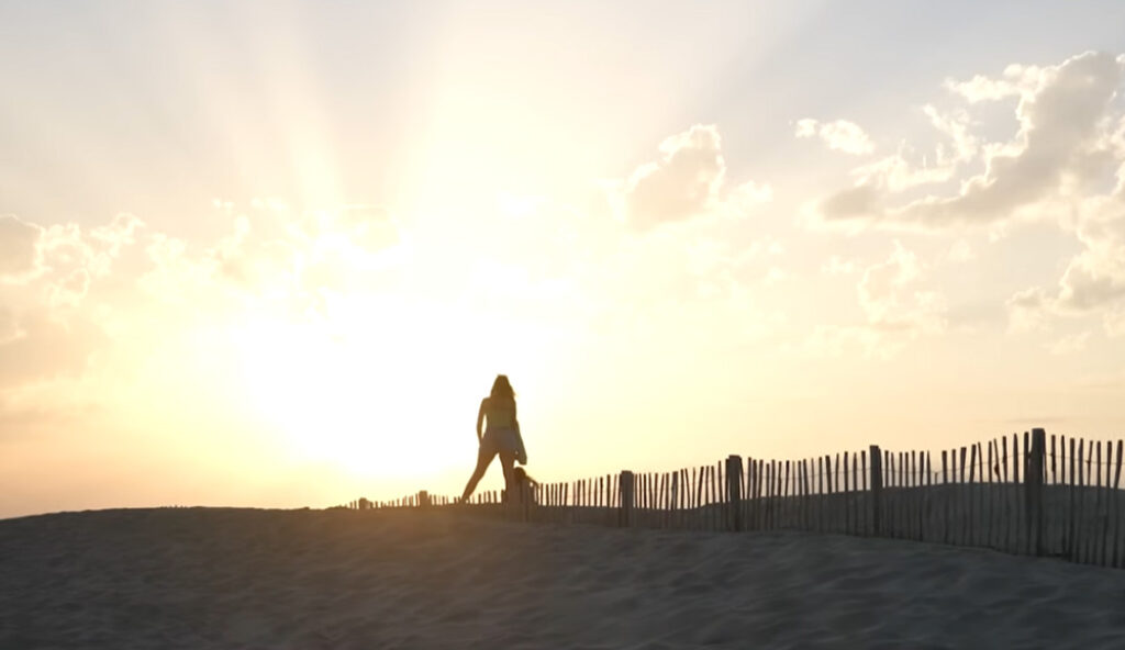 Silhouette de femme marchant sur une dune au coucher du soleil avec ganivelles sur une plage méditerranéenne en Occitanie