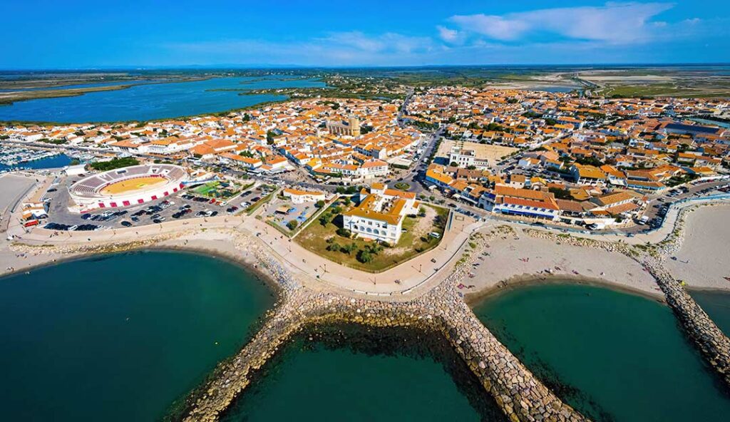 Vue aérienne des Saintes-Maries-de-la-Mer avec église fortifiée, plages, arènes et étang de Camargue en Provence