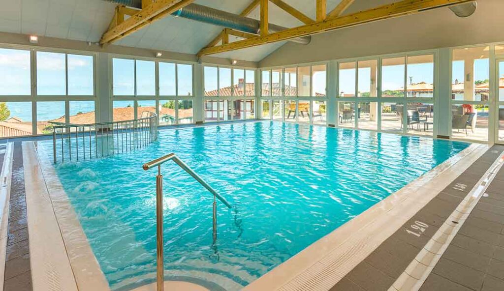 Piscine intérieure couverte hôtel Azureva avec grandes baies vitrées, charpente apparente et vue panoramique sur l'océan