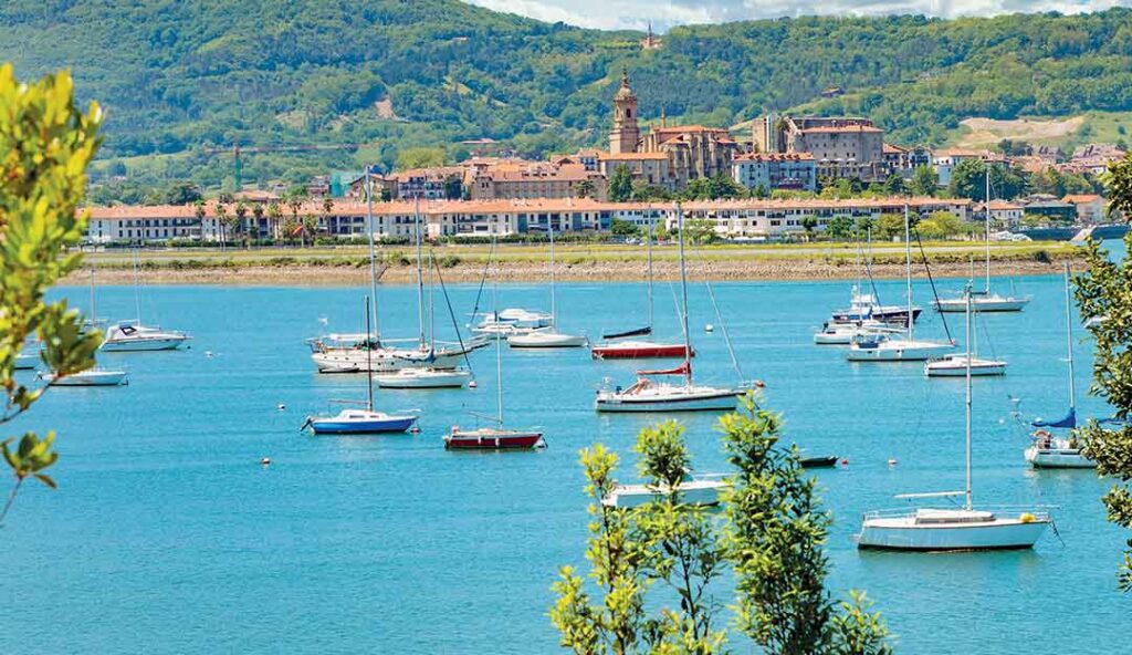 Village basque de Hondarribia en Espagne avec voiliers sur eaux turquoise, église et montagnes en arrière-plan