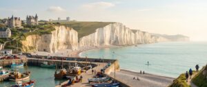 Vue ultra réaliste de la Côte d’Albâtre en Normandie avec falaises calcaires blanches, plages de galets, port de pêche de Fécamp, villas élégantes en arrière-plan, et activités de plein air sous une lumière douce printanière