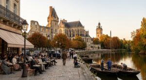 Vue réaliste des ruines du château des ducs de Bourbon à Moulins au coucher de soleil d’automne, avec la cathédrale Notre-Dame de l’Annonciation, la tour Jacquemart, une terrasse du Grand Café Belle Époque animée, et le fleuve Allier bordé de futreaux traditionnels