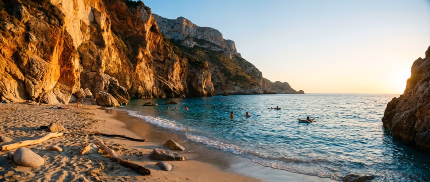 Coucher de soleil sur une plage sauvage de Sardaigne avec falaises dorées, mer cristalline et quelques baigneurs